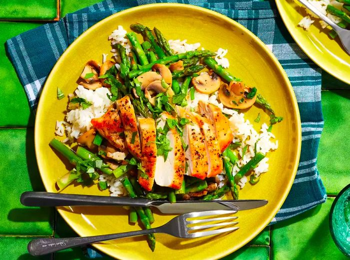 An overhead view of chicken, asparagus, and mushrooms served on a plate of steamed white rice.