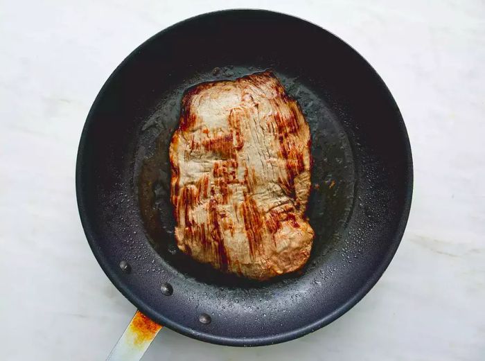 Searing flank steak in a skillet.