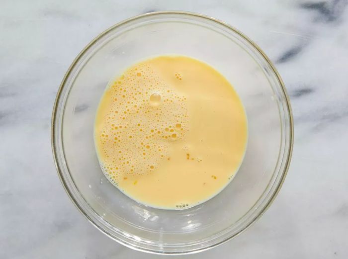 A top-down view showing whisked evaporated milk and eggs blended together in a bowl until smooth.