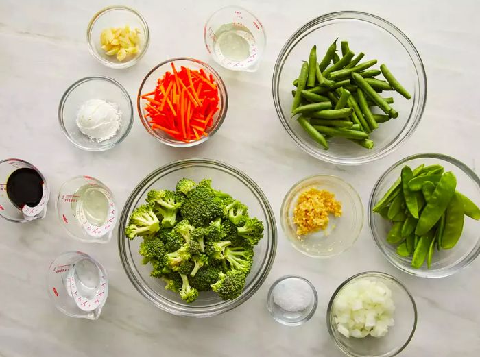 A top-down view of stir-fry ingredients arranged in various bowls and measuring cups.