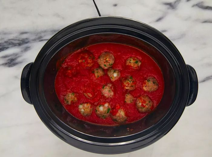 Aerial view of a slow cooker filled with tomato sauce and meatballs, ready to cook