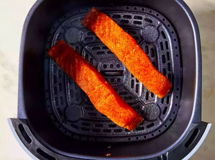 Two well-seasoned salmon fillets placed in the basket of an air fryer.