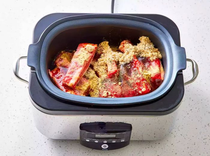 Spare ribs arranged in the slow cooker with all the ingredients added.