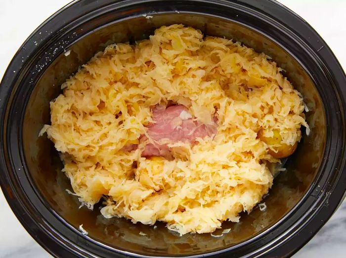 The pork tenderloin is placed in the slow cooker with potatoes surrounding it and sauerkraut layered on top.