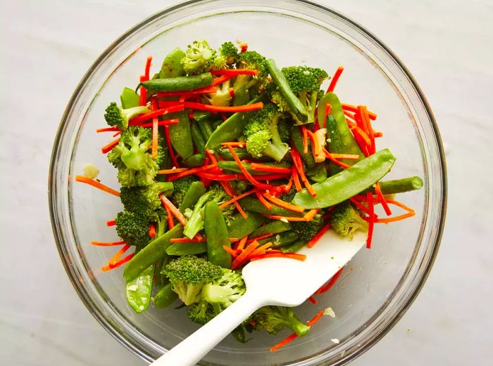 A top-down view of vegetables being mixed with a butter and garlic blend in a bowl.