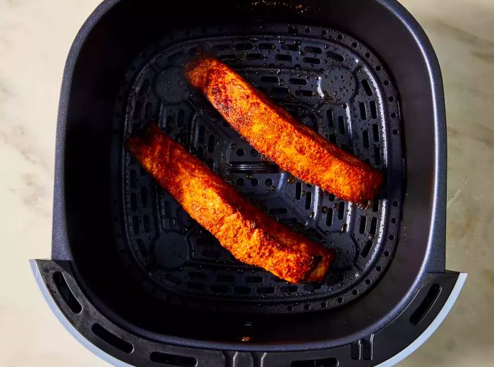 Two perfectly cooked salmon fillets in the air fryer basket.