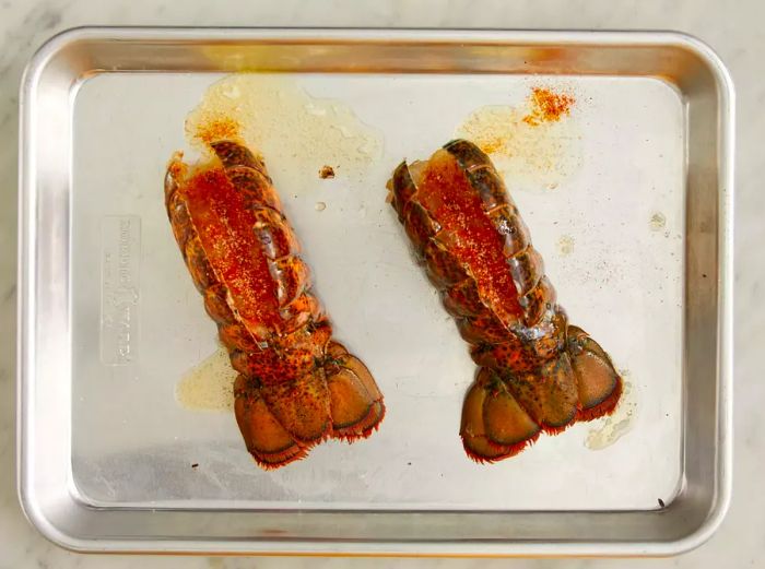 A top-down view of uncooked lobster tails seasoned and placed on a baking sheet.