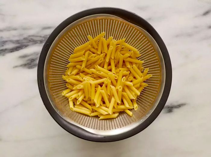 A colander filled with drained, cooked penne pasta