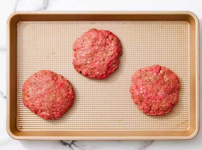 Raw hamburger patties arranged on a baking sheet