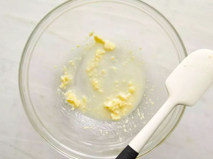 A top-down view of butter and garlic being blended together in a glass bowl.