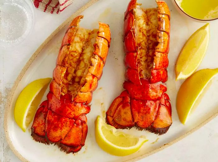 A top-down view of two broiled lobster tails, beautifully garnished with lemon wedges.