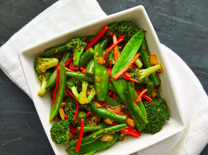 A top-down view of a bowl filled with ginger veggie stir-fry, featuring snow peas and broccoli.