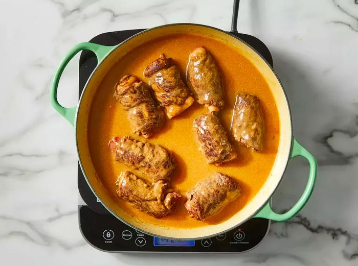 A top-down view of beef rouladen being added back into the pan with the sauce