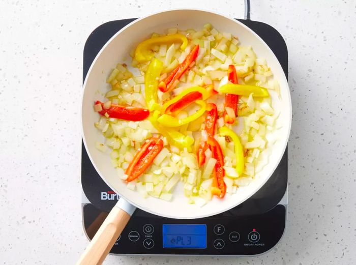 Onions and bell peppers sautéing in a skillet