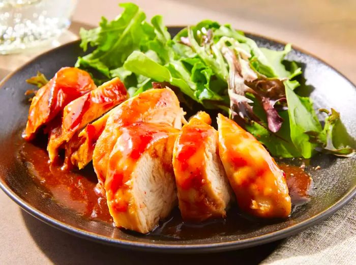 A sliced serving of slow cooker BBQ chicken on a plate, accompanied by a fresh salad.