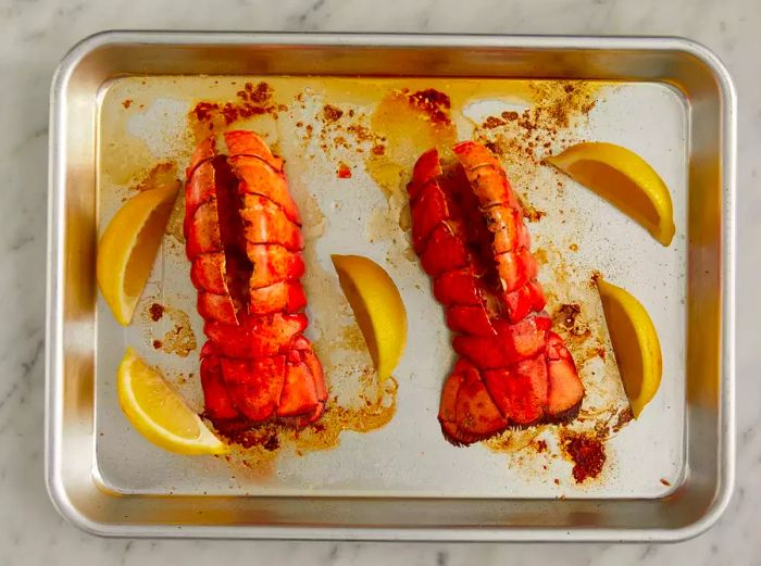 A top-down view of broiled lobster tails on a baking sheet, garnished with lemon wedges.