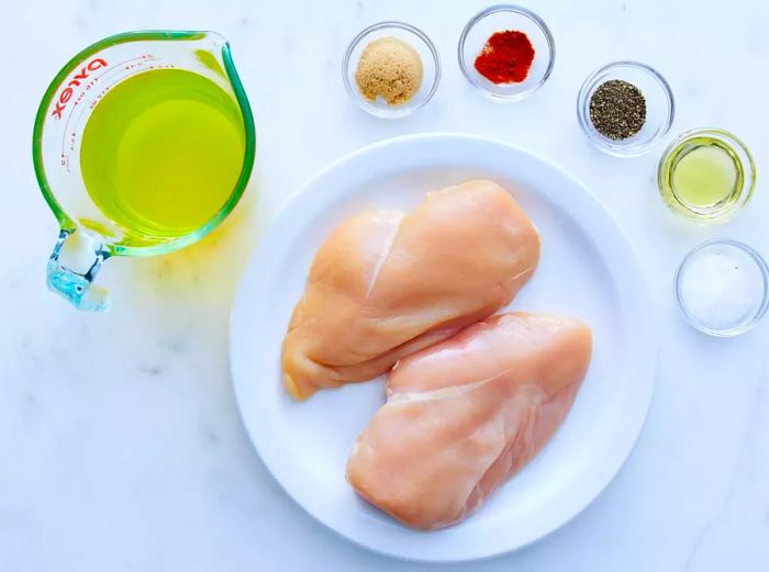 Raw chicken pieces surrounded by spices and oil in glass bowls