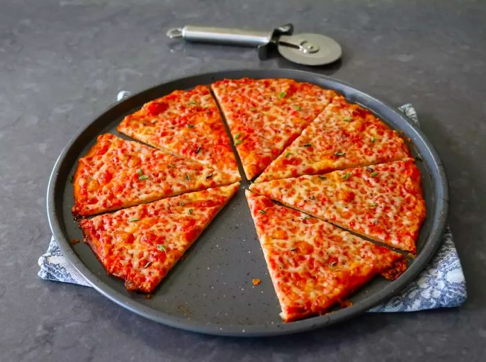 Pizza with red sauce, cut into triangles, with one slice missing and a pizza cutter in the background.