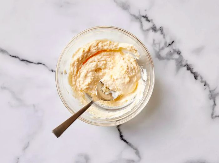 A bowl of Parmesan cheese and mayonnaise being mixed together with a spoon