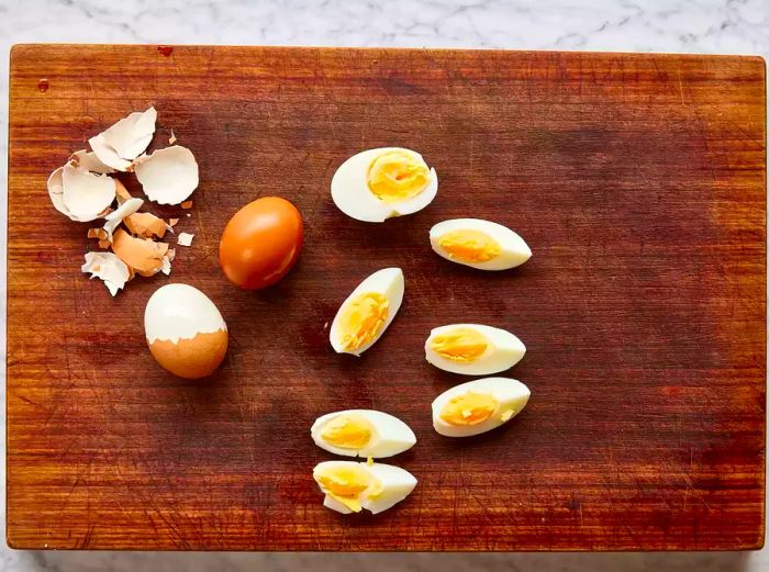 A cutting board with peeled hard-boiled eggs, two of which are cut into quarters