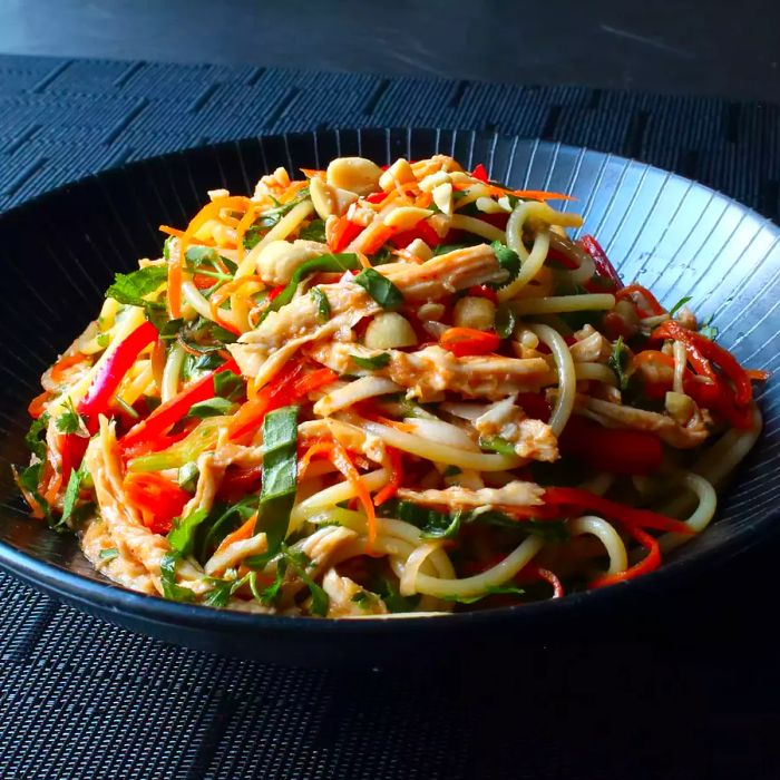 Close-up of Chicken Noodle Salad featuring peppers, carrots, and lettuce in a black bowl