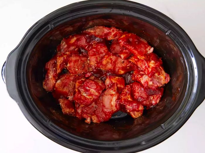 A slow cooker filled with seasoned pork rib tips smothered in BBQ sauce and liquid smoke blend