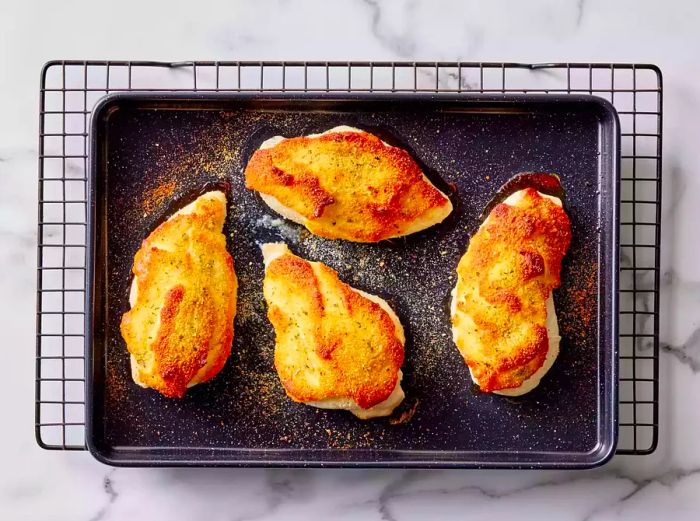 A baking sheet with four crispy Parmesan-crusted chicken breasts