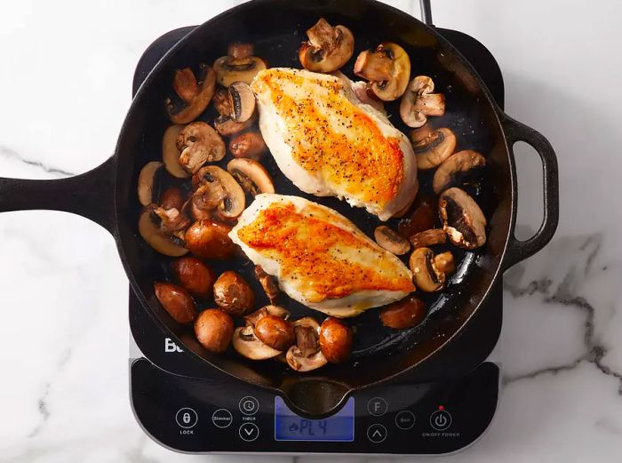 Chicken and mushrooms browning together in the skillet.