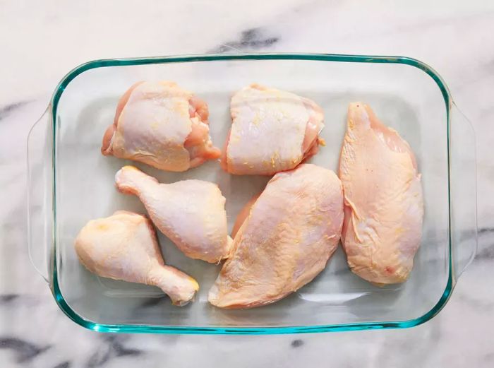 A baking dish containing chicken thighs, breasts, and drumsticks.