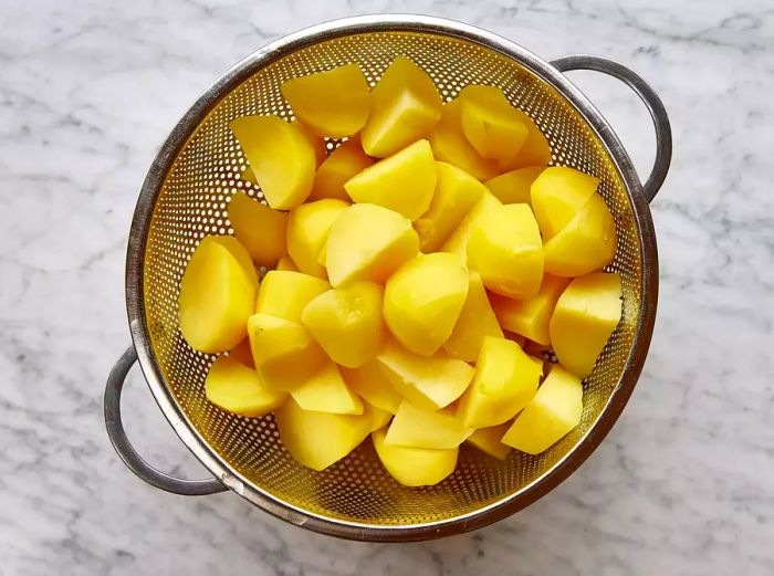 A metal colander filled with chopped boiled potatoes