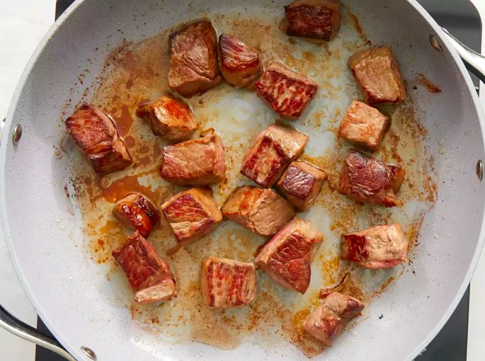 A top-down view of steak cuts cooking in a skillet.