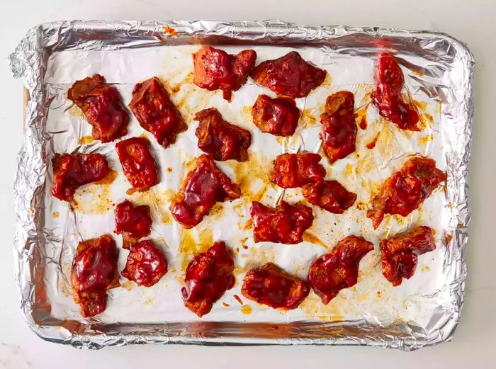 A baking sheet lined with foil, featuring slow-cooked pork ribs smothered in barbecue sauce