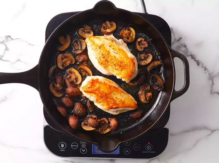 Chicken and mushrooms browning together in the skillet.