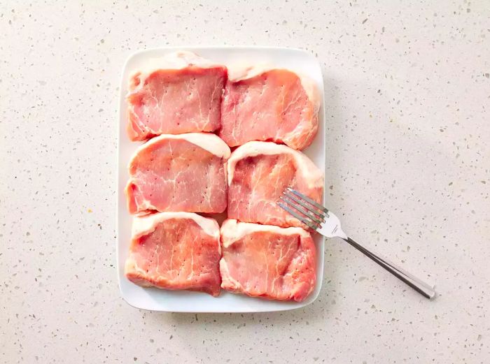 Pork chops arranged on a white platter with a fork beside them