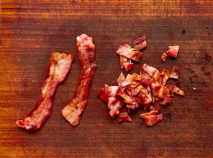 A cutting board with two whole slices of crispy bacon alongside a small pile of chopped bacon