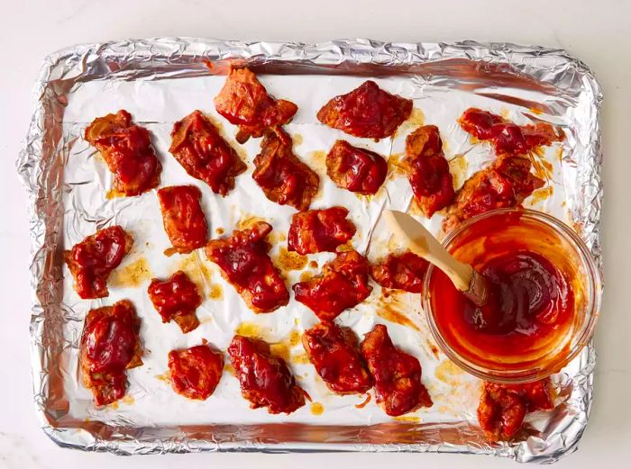 A foil-lined baking sheet with slow-cooked pork rib tips brushed with additional barbecue sauce