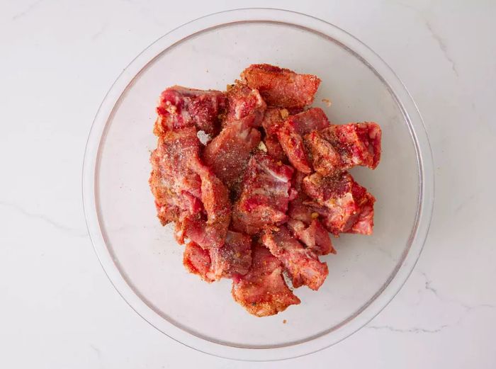 A glass bowl filled with pork rib tips coated in spice mix