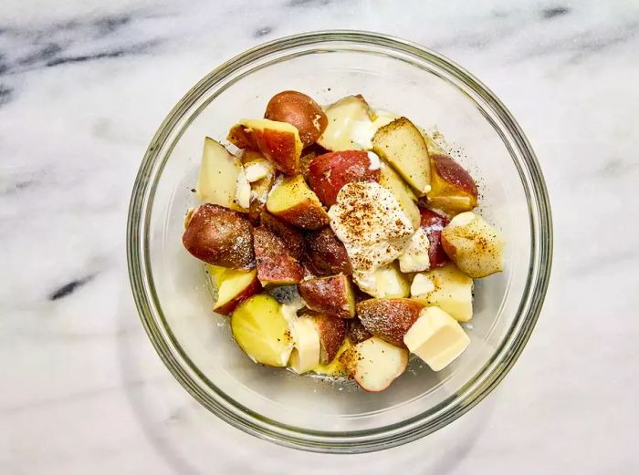 A large bowl filled with boiled and quartered red potatoes, milk, butter, sour cream, salt, and pepper.