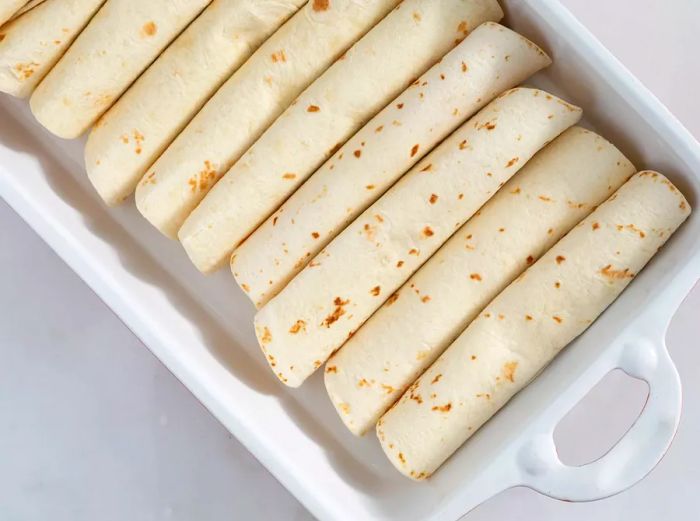 Rolled tortillas placed neatly in the baking dish