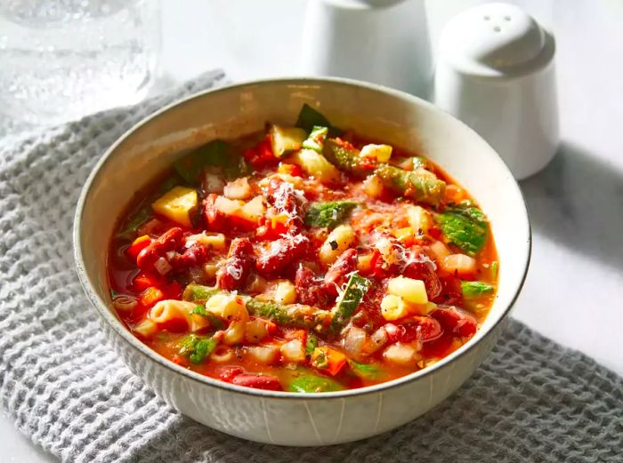 A top-down view of a bowl of slow cooker vegetarian minestrone soup, garnished with Parmesan cheese.