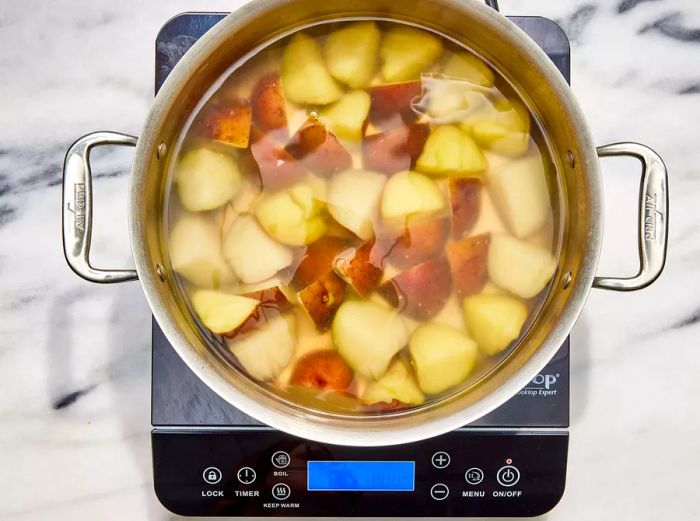 A large pot filled with quartered red potatoes submerged in water