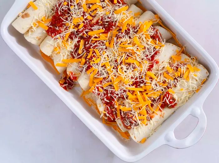 Enchiladas rolled and placed in a baking dish, topped with cheese mixture, salsa, and green onions