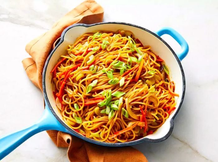 overhead view of a skillet with lo mein noodles topped with green onions