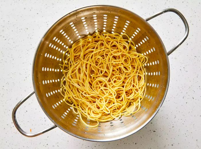 spaghetti noodles being drained in a colander