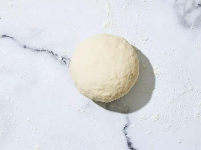 A top-down view of dough shaped into a ball on a floured surface.