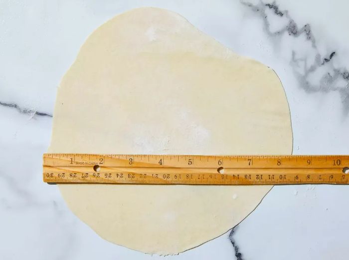 A top-down view of flattened dough on a work surface, stretched to about 8 inches in diameter.