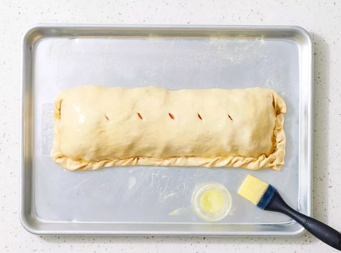 A baking sheet with an unbaked stromboli, coated in butter