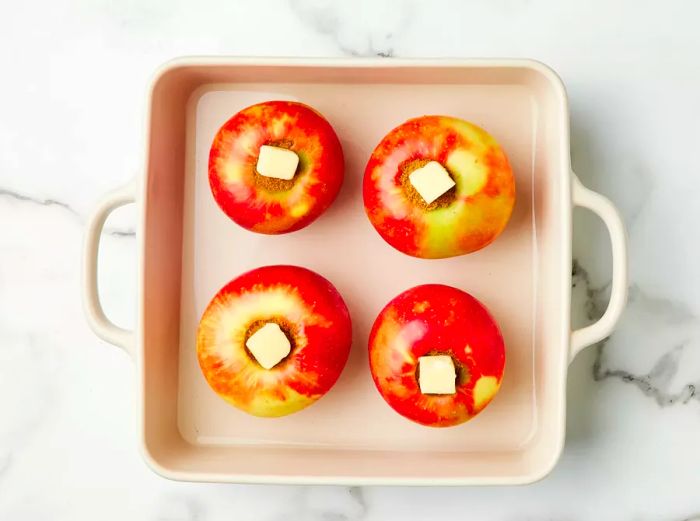 Apples topped with butter and arranged in a baking dish