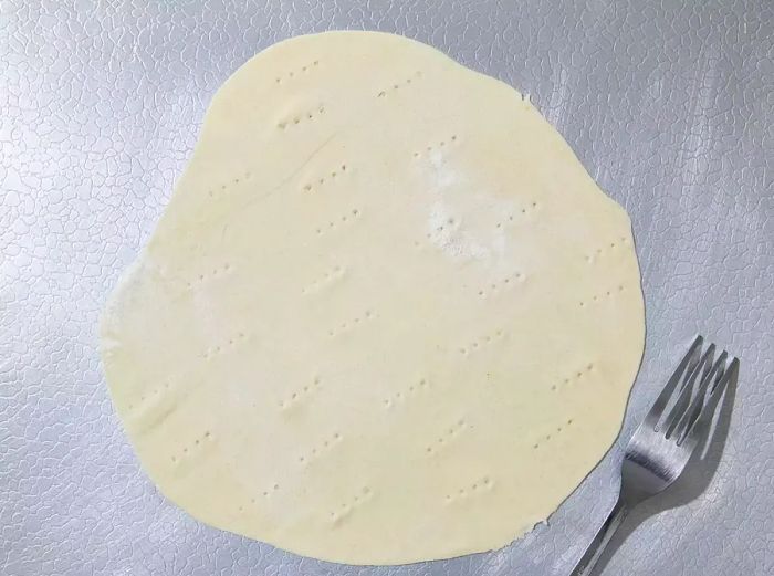 A top-down shot of flattened dough pierced with a fork.