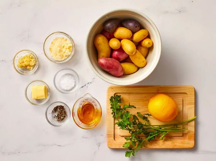 A collection of ingredients for garlic Parmesan fingerling potatoes arranged on a clean, white surface.